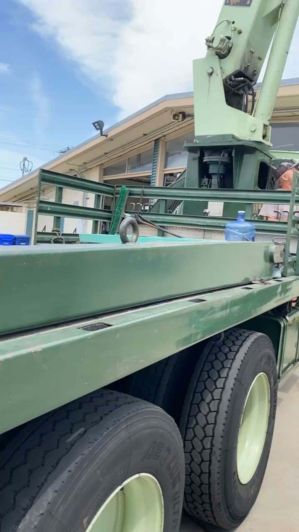 Green truck with large crane arm parked outside, showcasing sturdy tires and loading area.
