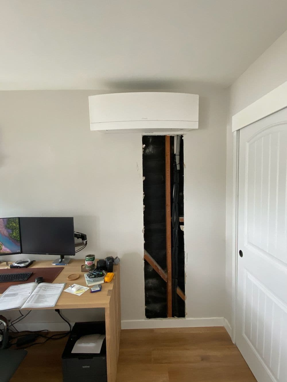 Wall-mounted air conditioner above a cut-out section, with a desk and computer nearby.