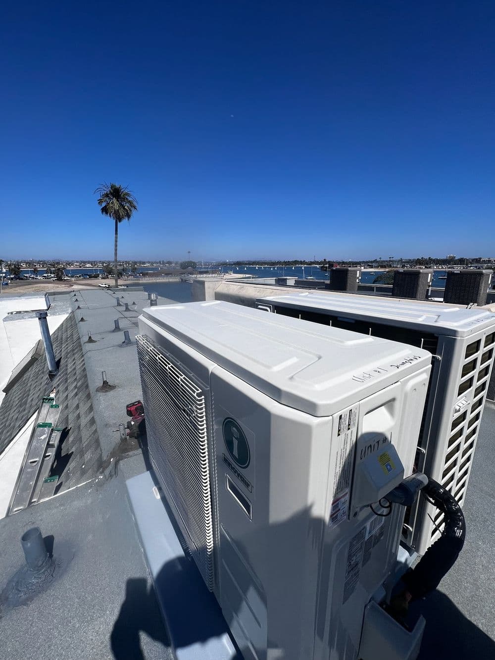 Air conditioning units on a rooftop with a clear blue sky and palm trees in the background.