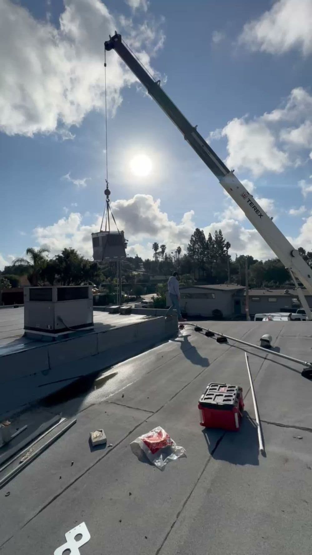 Crane lifting equipment on a rooftop under a sunny sky with scattered clouds.