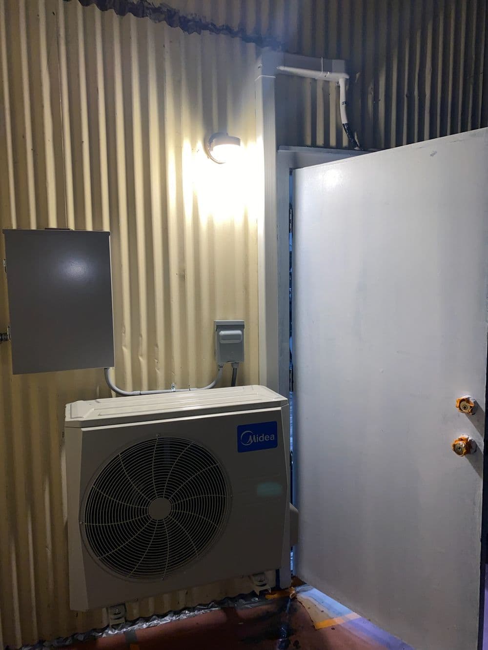 Midea air conditioning unit mounted indoors next to an open door in a metal-walled room.