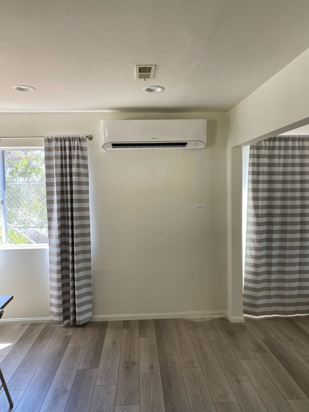 Modern living room with air conditioning unit, large window, and striped curtains.