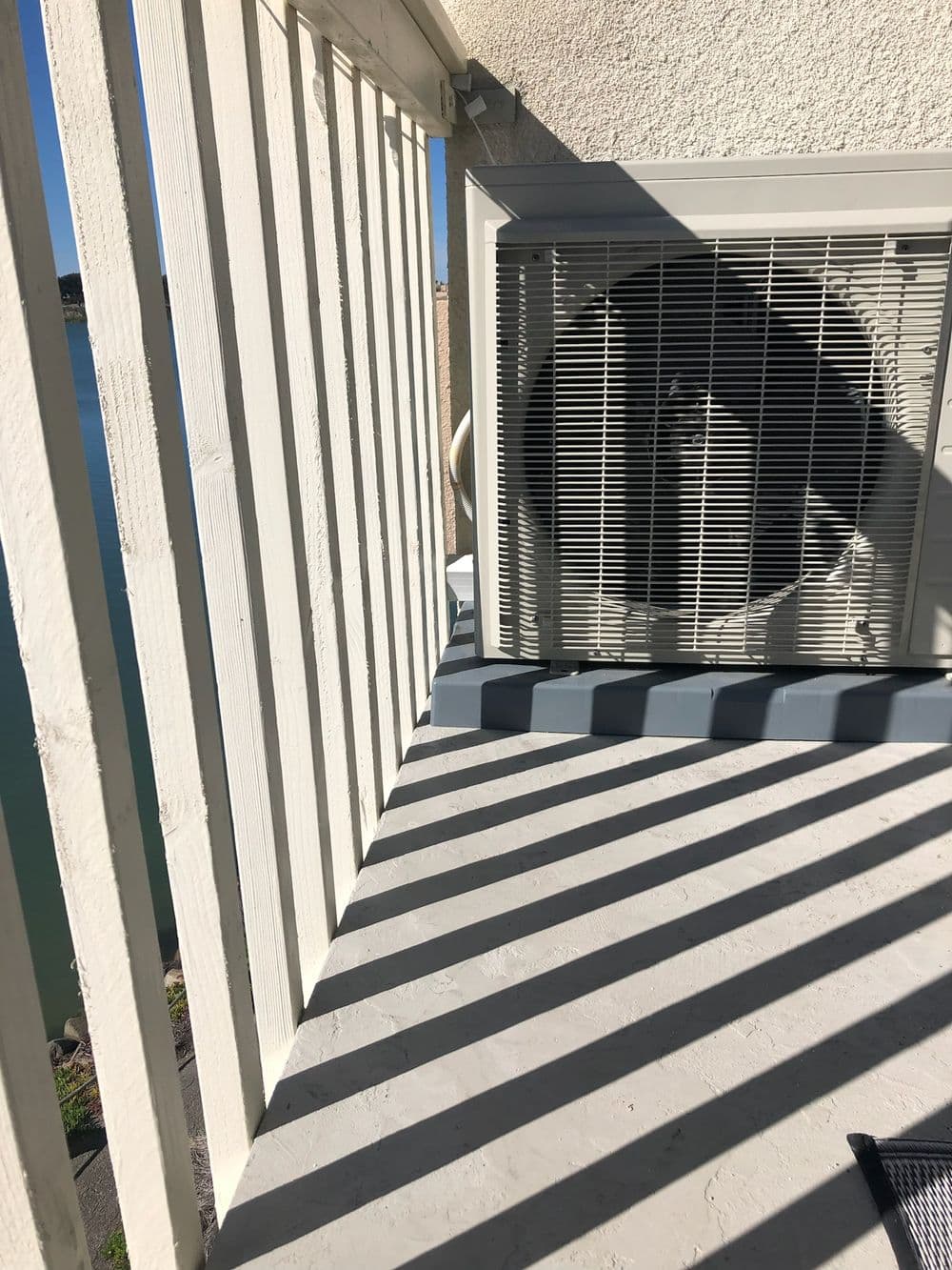 Air conditioning unit installed on a balcony with shadows cast by railings and a clear view.