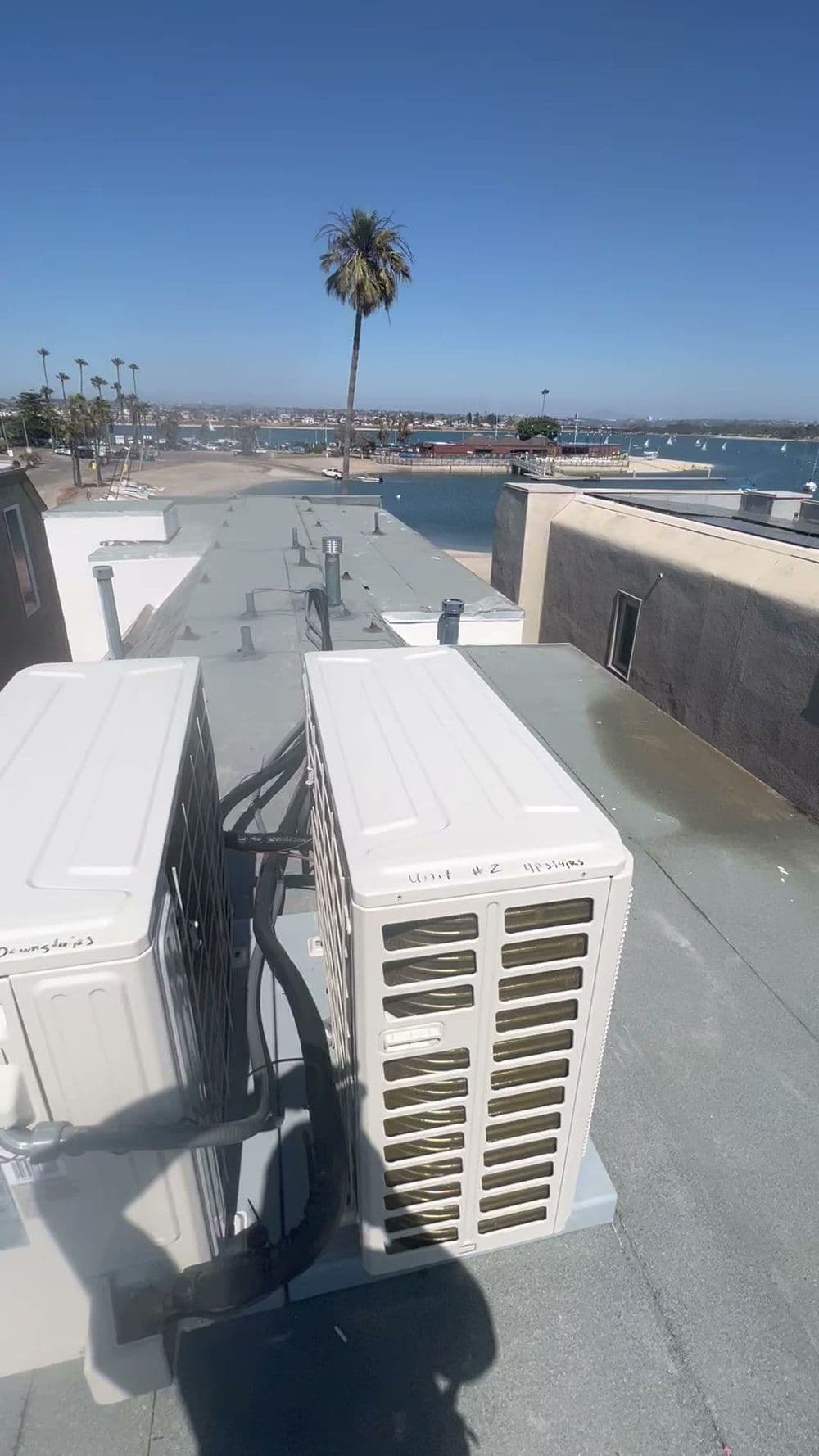 Rooftop view with air conditioning units overlooking a waterfront and palm trees.