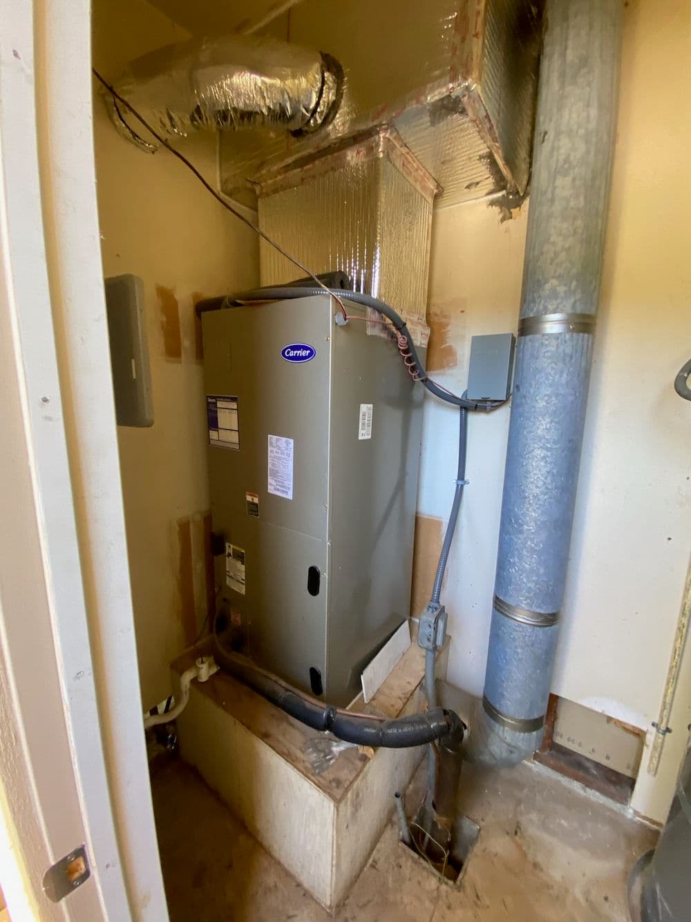 Furnace installation in a utility closet with ductwork and piping for heating system.