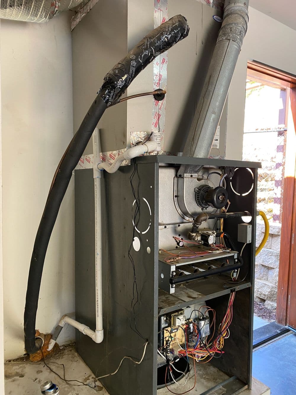Furnace system with ductwork and wires exposed in residential utility room.