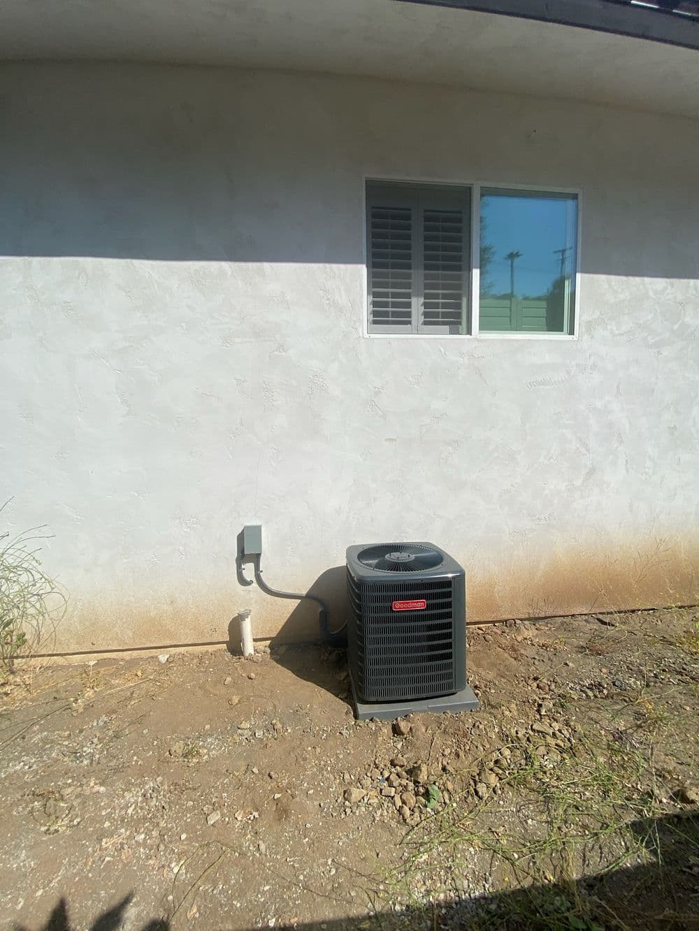 New air conditioning unit installed next to a house, with a window in the background.
