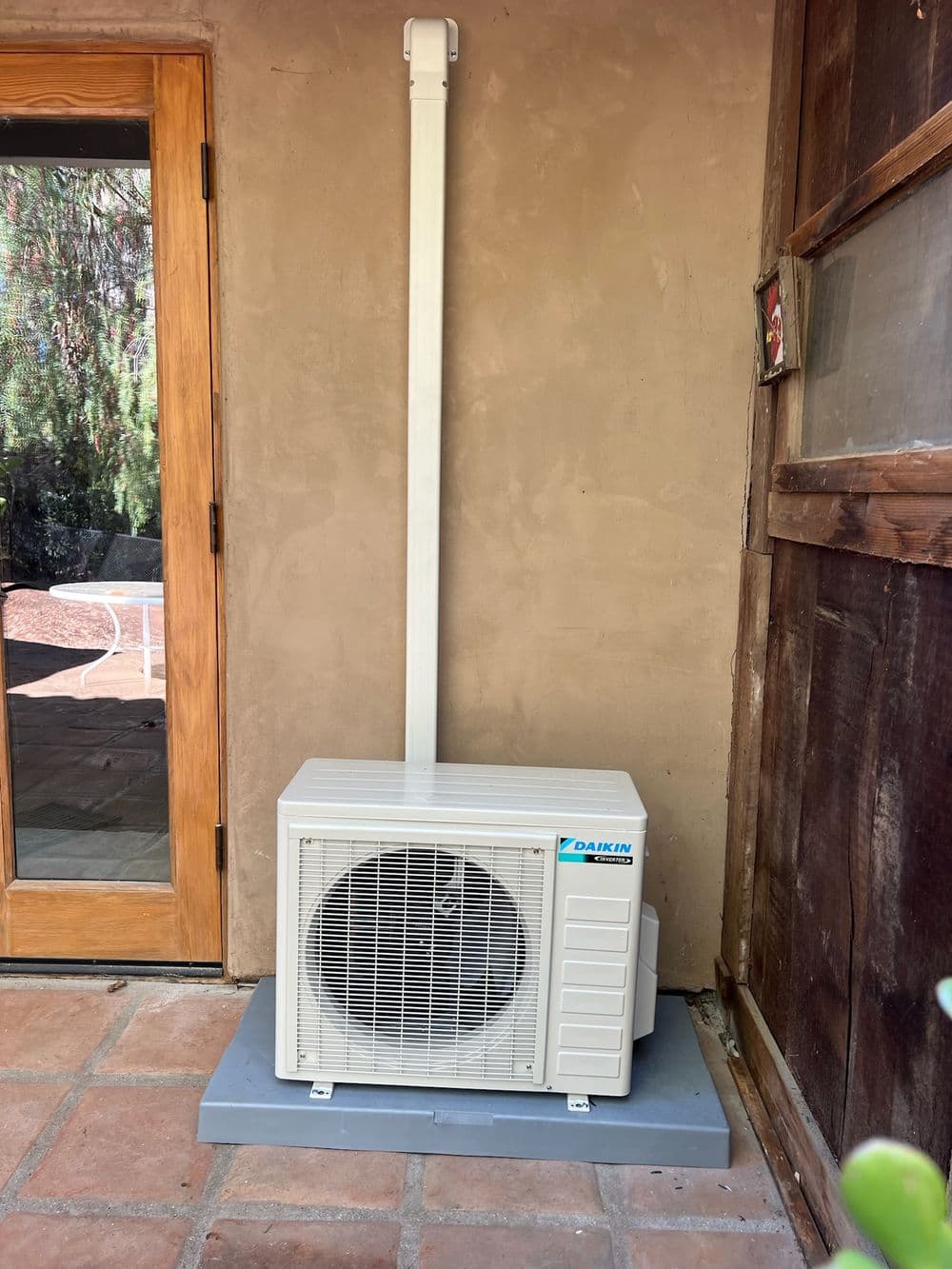 Daikin outdoor air conditioning unit installed beside wooden door on patio.