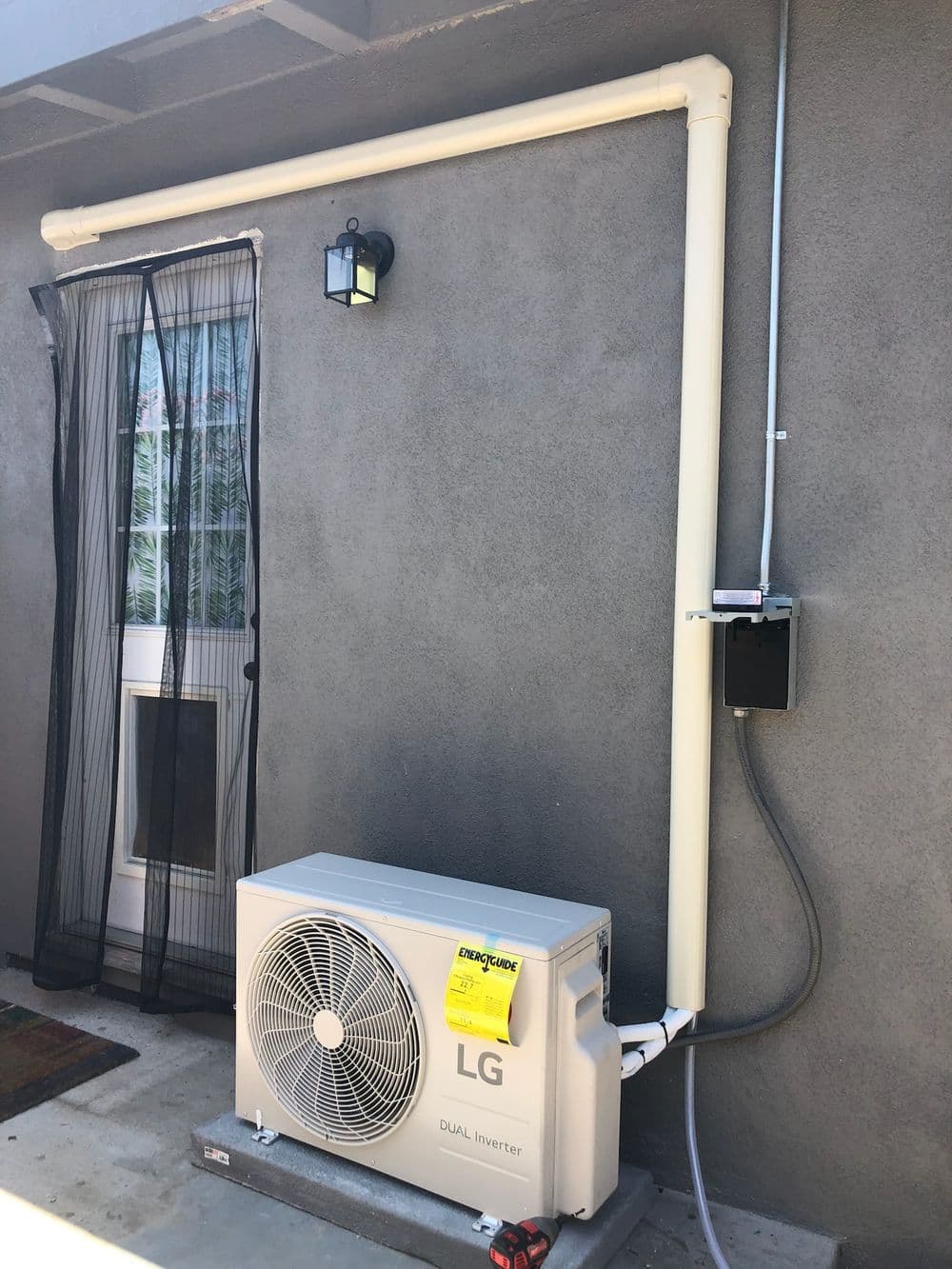 LG dual inverter air conditioning unit mounted on a gray wall with piping and electrical connection.