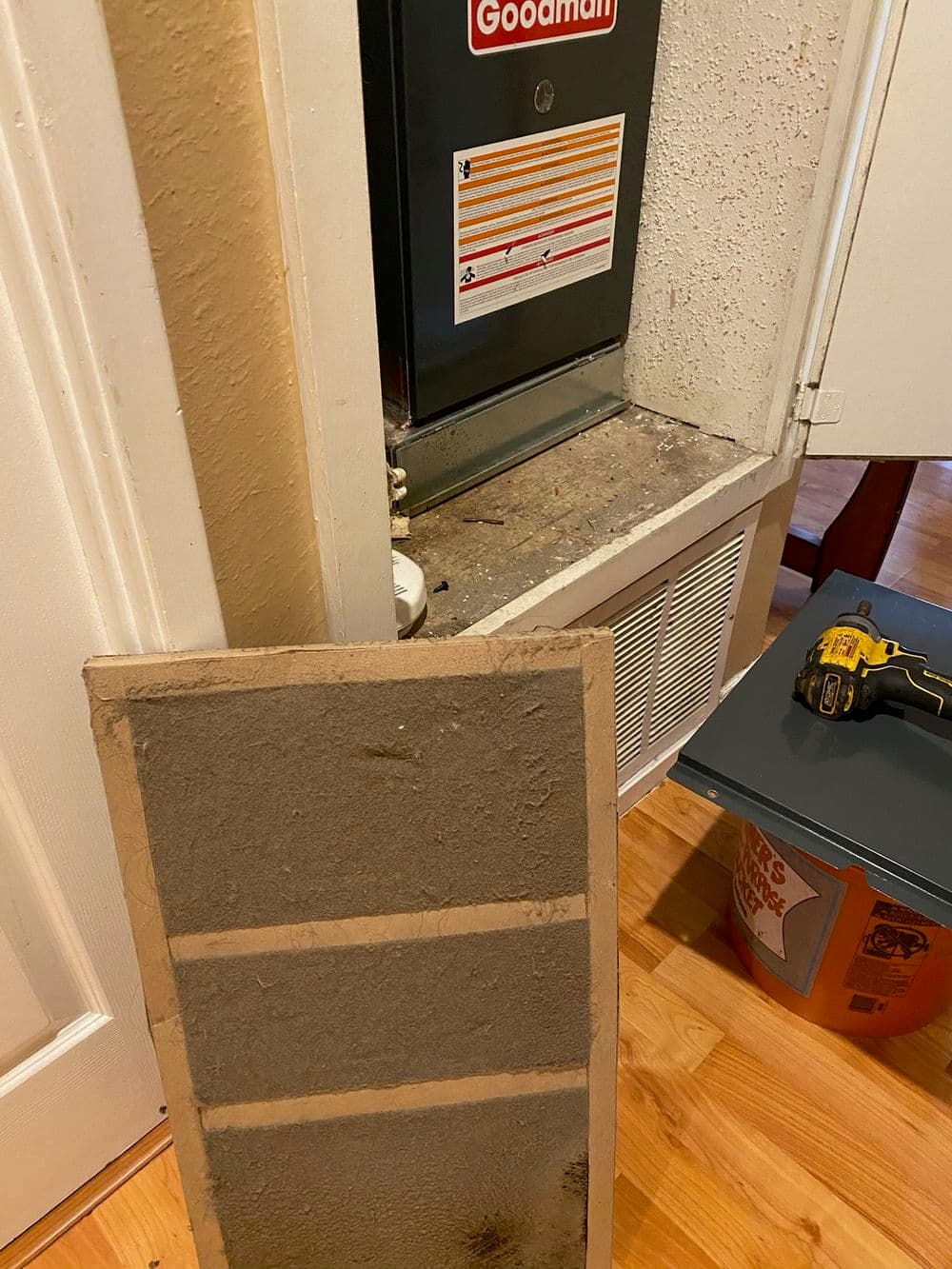 Goodman HVAC unit with nearby panel and tools on wooden floor in residential space.