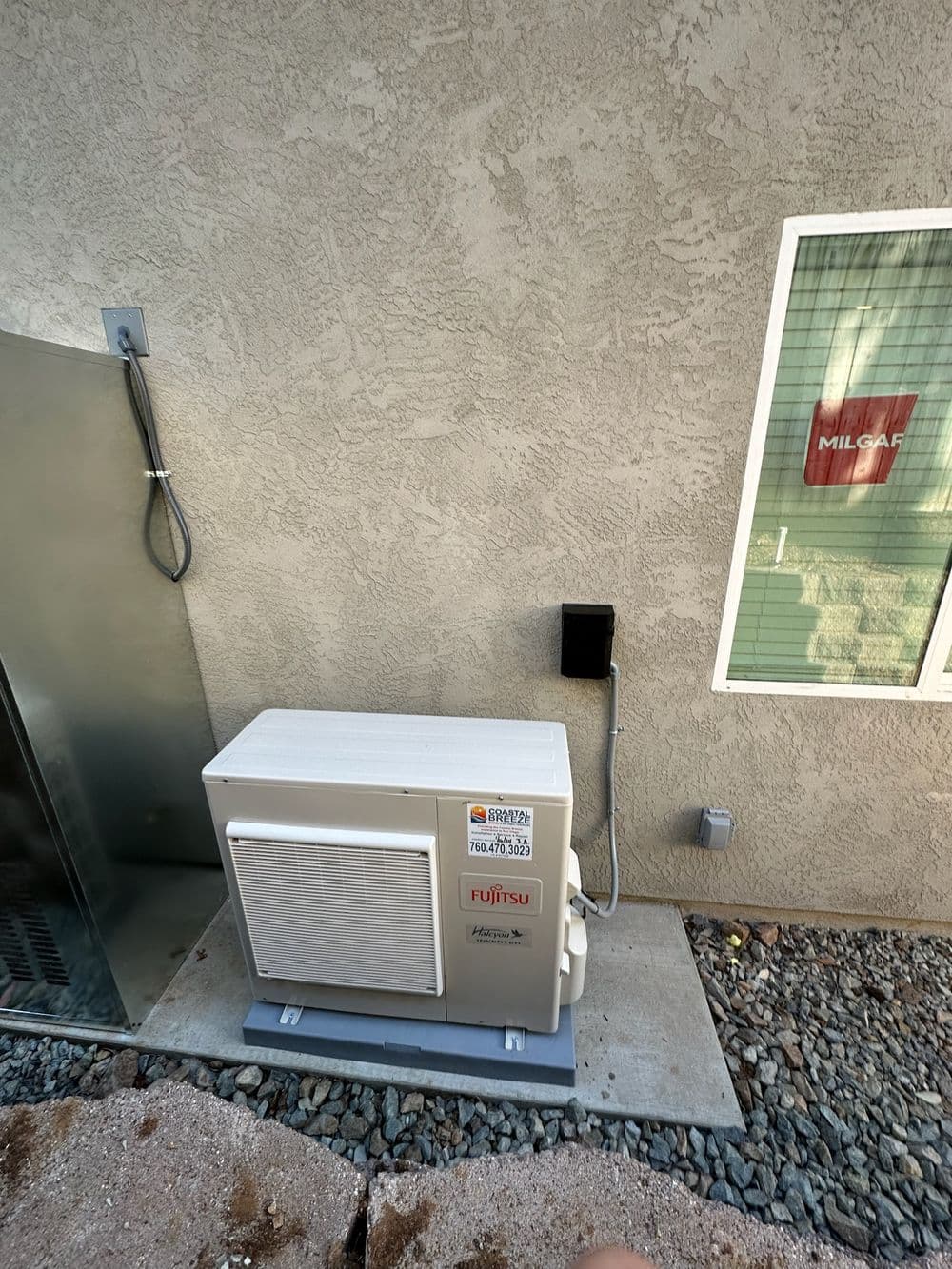 Fujitsu outdoor AC unit installed beside a textured wall near a window.