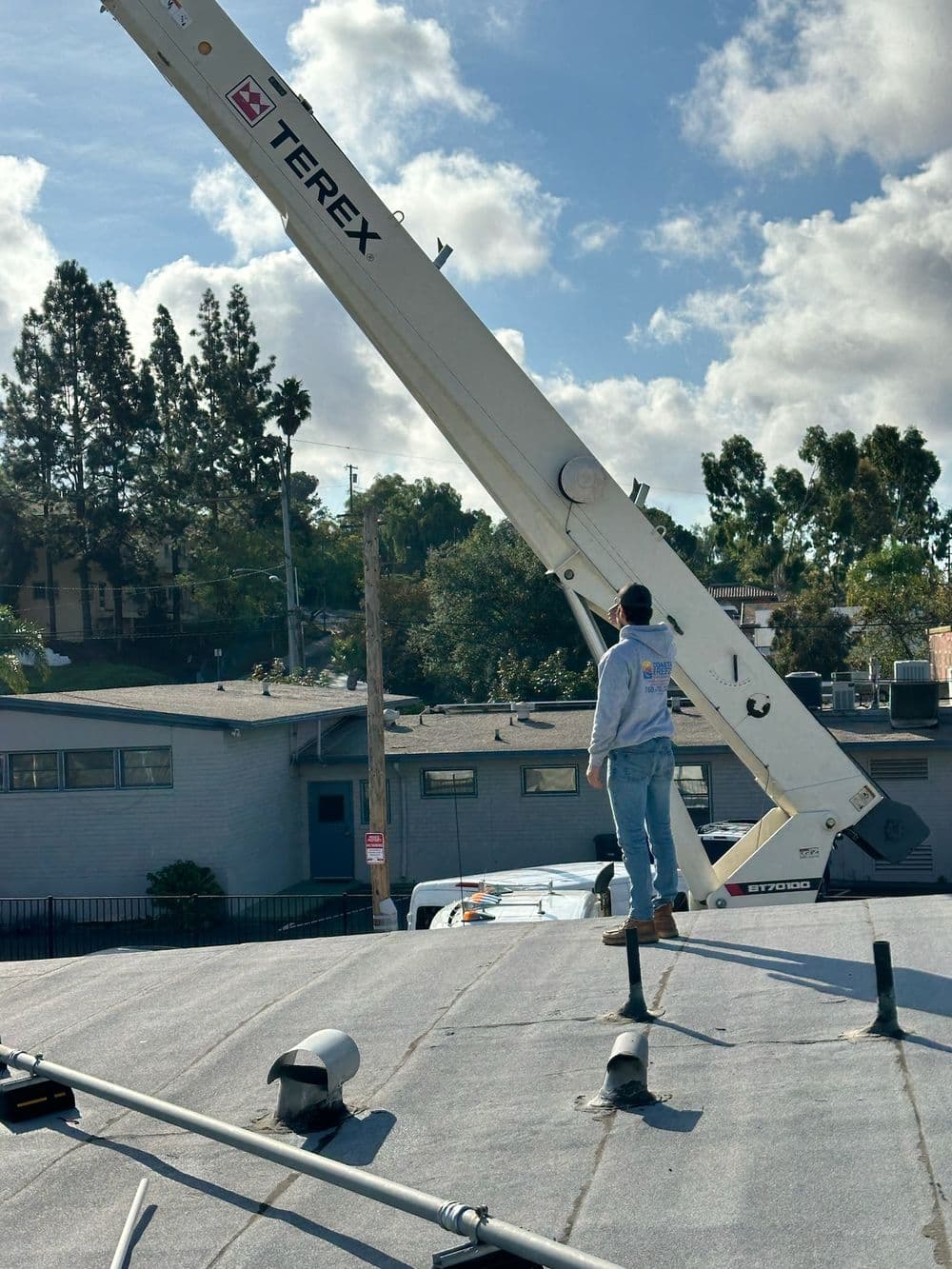 Person operating a Terex crane on a roof, with bright skies and trees in the background.