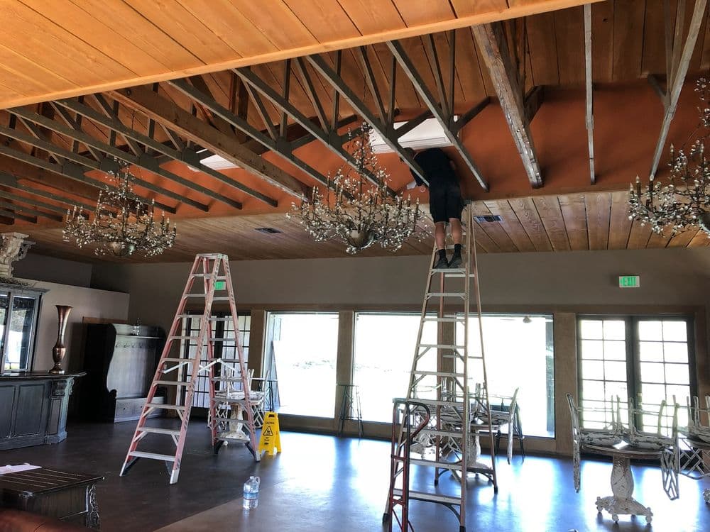 Worker on ladder performing maintenance in a spacious, elegant venue with chandeliers.