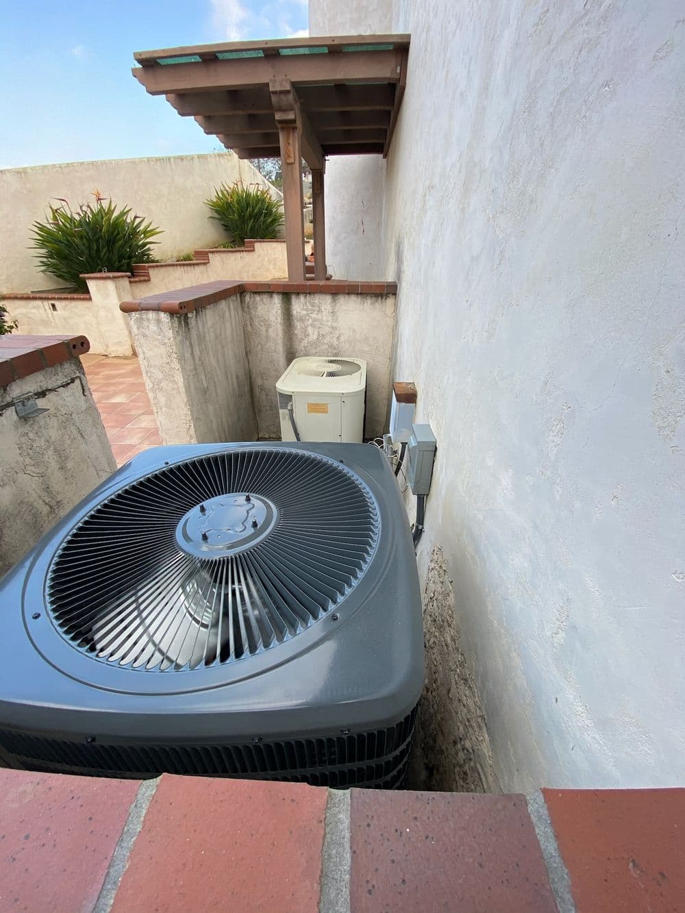 Air conditioning units positioned beside a wall in a residential outdoor space.