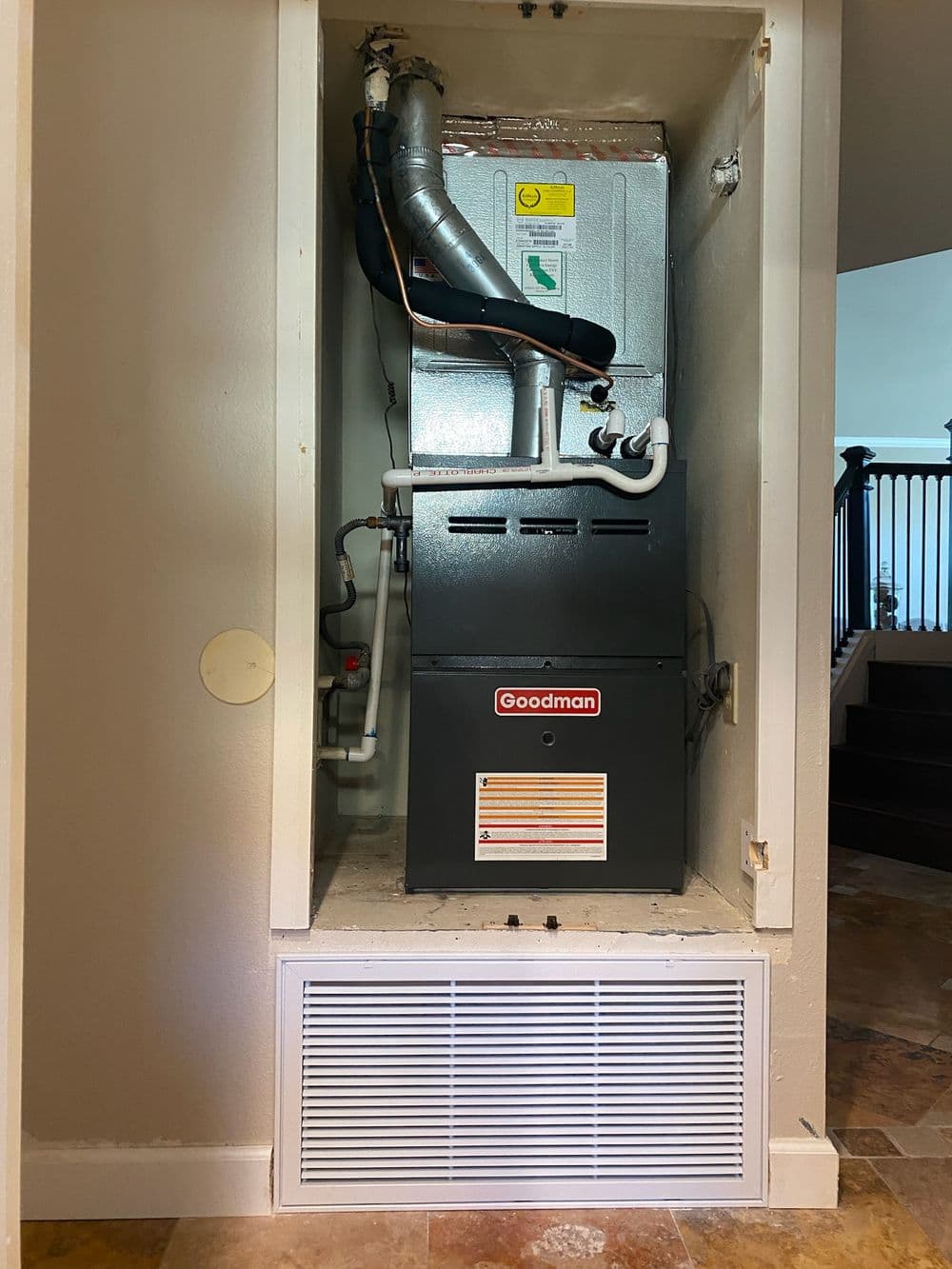 Goodman furnace installed in wall-mounted enclosure with ventilation grille beneath.