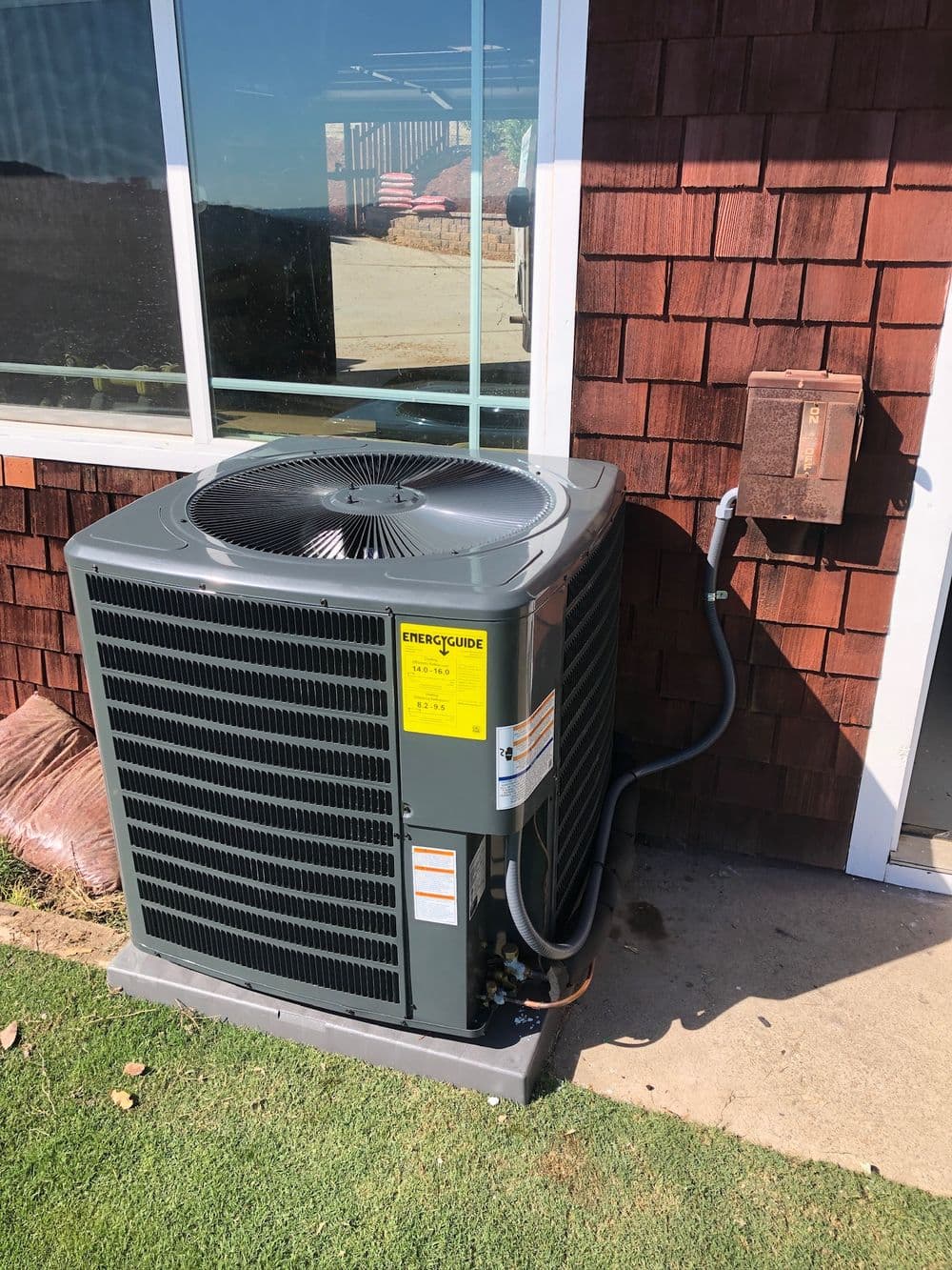Air conditioning unit installed next to a wooden house with a power connection.