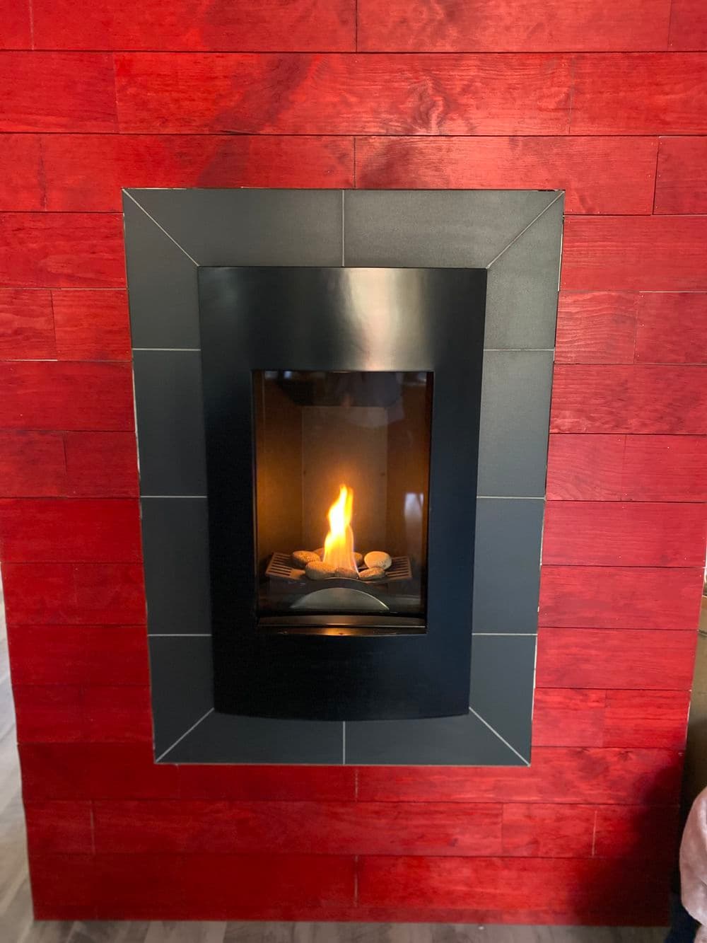 Modern fireplace with black frame and red wooden wall backdrop, showcasing a warm flame.