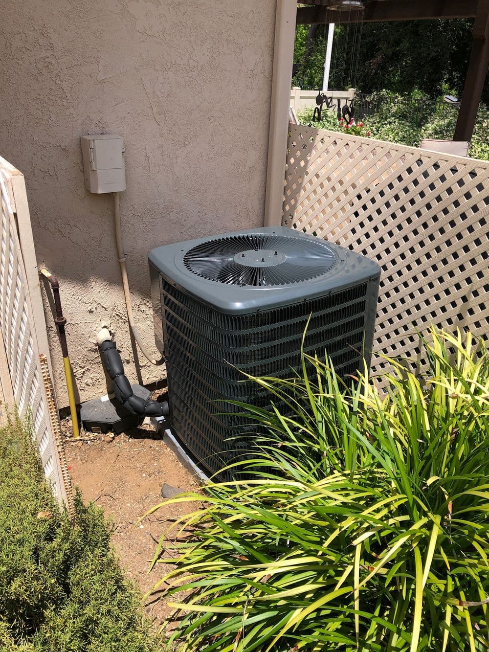 Air conditioning unit beside a house, surrounded by greenery and a privacy fence.
