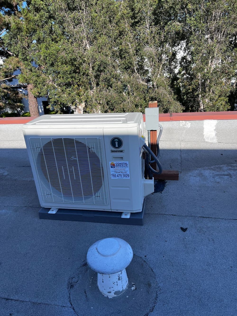 HVAC unit on a rooftop with greenery in the background and a ventilation pipe.