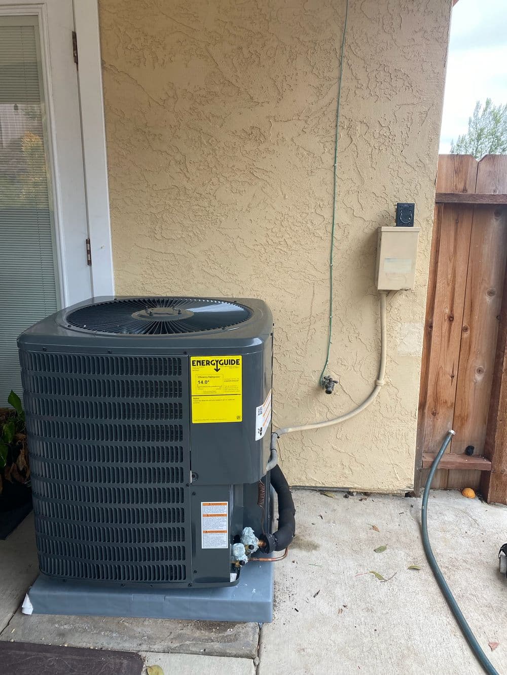 Air conditioning unit installed outside a house, featuring a gray exterior and EverGuide label.