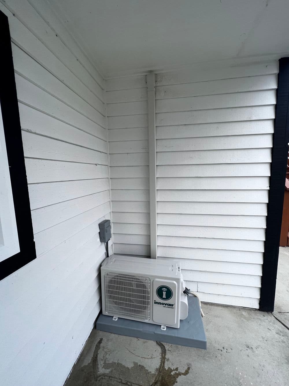 Air conditioning unit mounted on a white wooden wall with gray flooring and electrical connections.