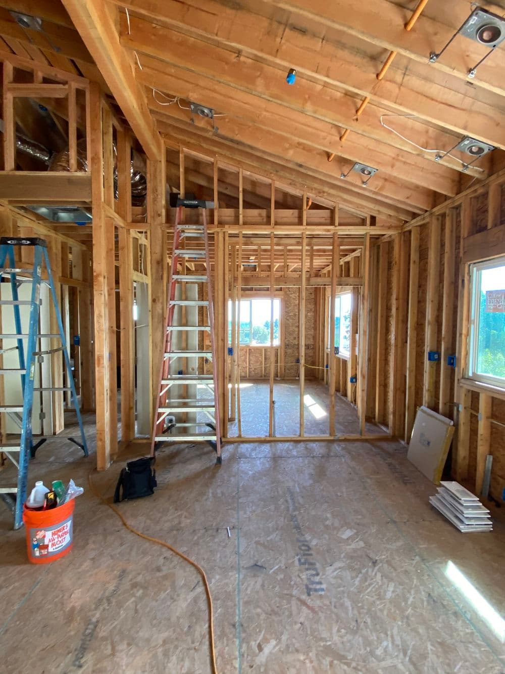 Interior of a home under construction, featuring wooden framing, ladders, and windows.