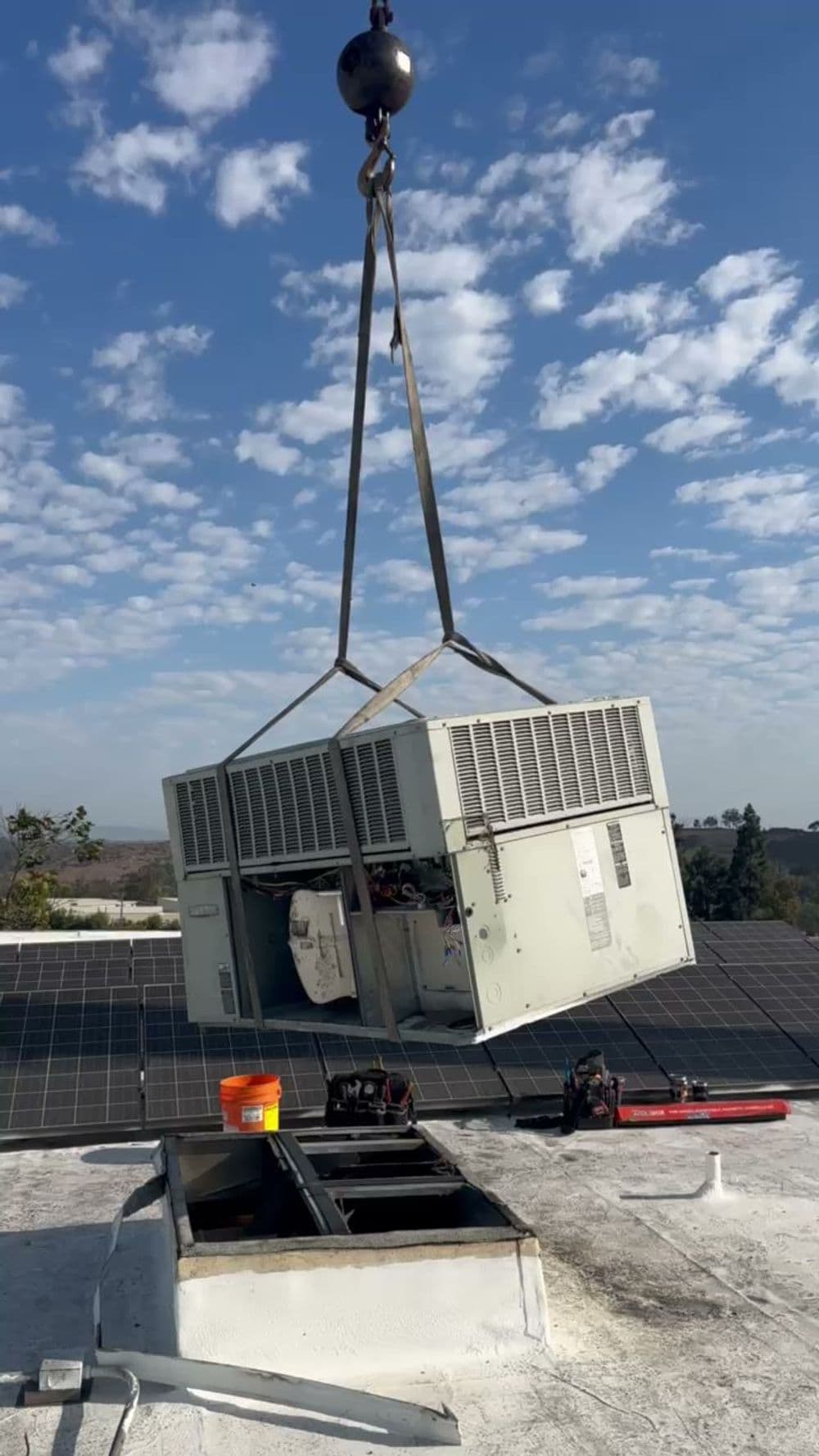 Air conditioning unit being lifted for installation on a rooftop with solar panels.