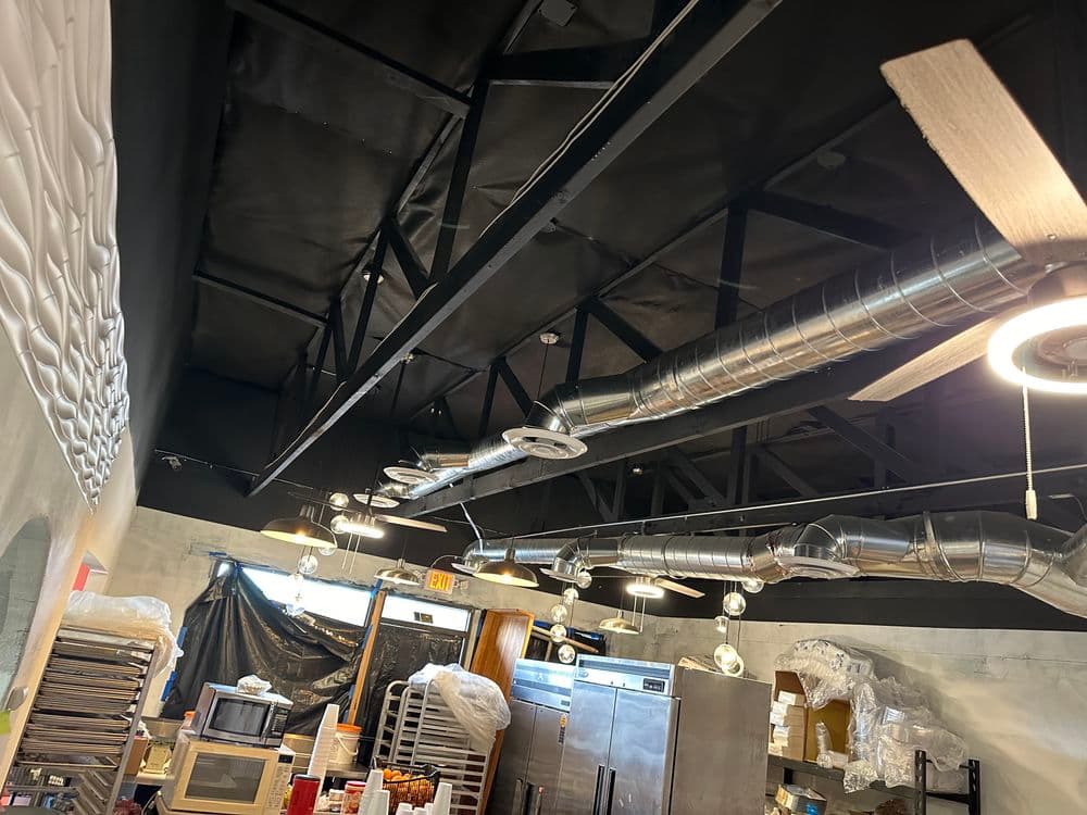 Interior view of a commercial kitchen featuring black ceilings and metal ventilation ducts.