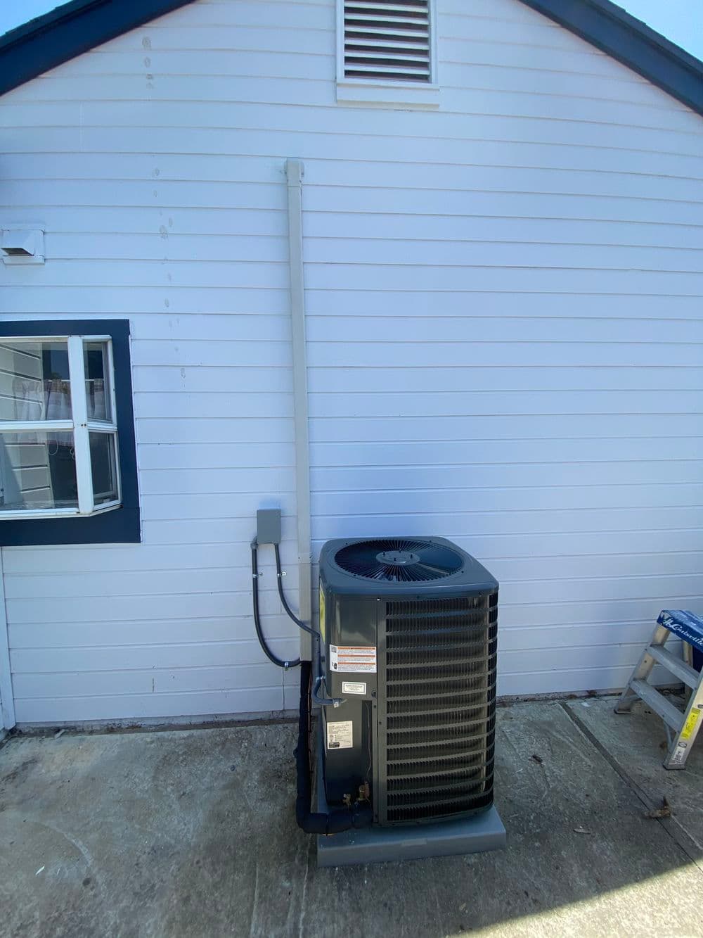 Air conditioning unit installed on exterior wall of a building, with service connections visible.