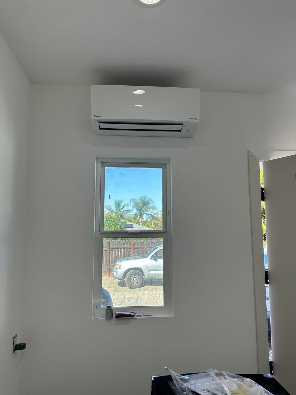 Modern air conditioner mounted above a window in a bright, minimalist room.