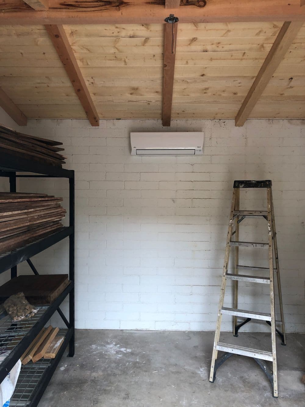 Interior of a workshop with wooden shelves, ladder, and wall-mounted air conditioner.