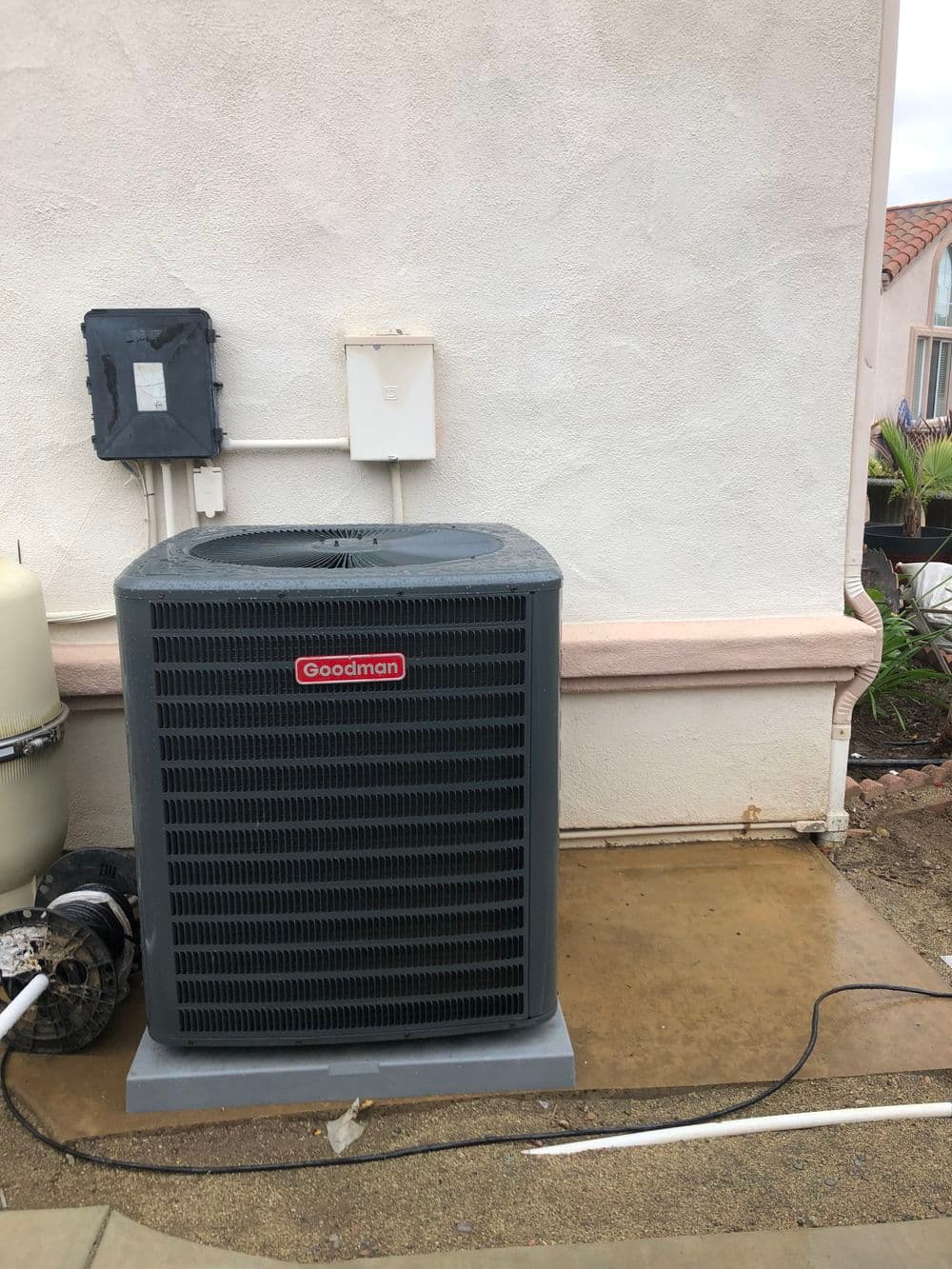 Goodman outdoor air conditioning unit installed beside a house on a concrete slab.