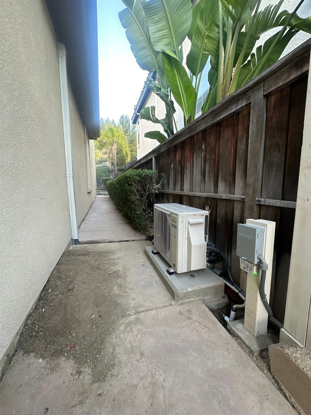 Air conditioning unit installed beside a house with greenery and concrete path.