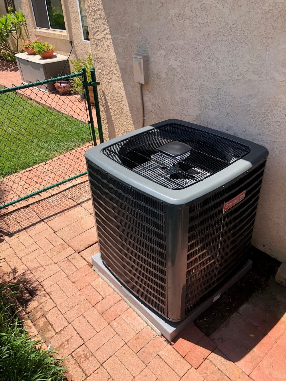 Air conditioning unit beside a garden path with a fence and lush greenery.