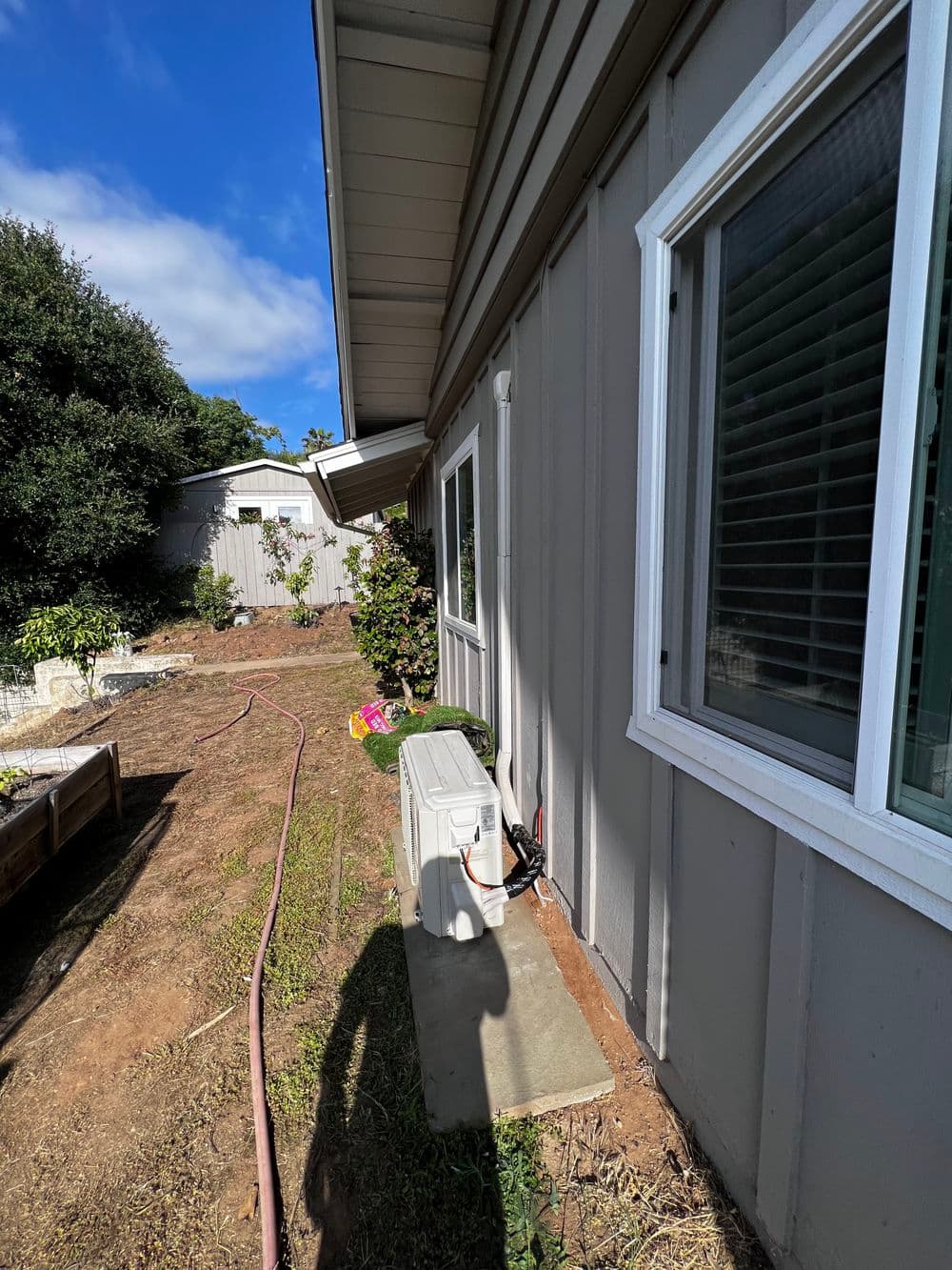 Side view of a house showing an air conditioning unit and garden area. Blue sky backdrop.