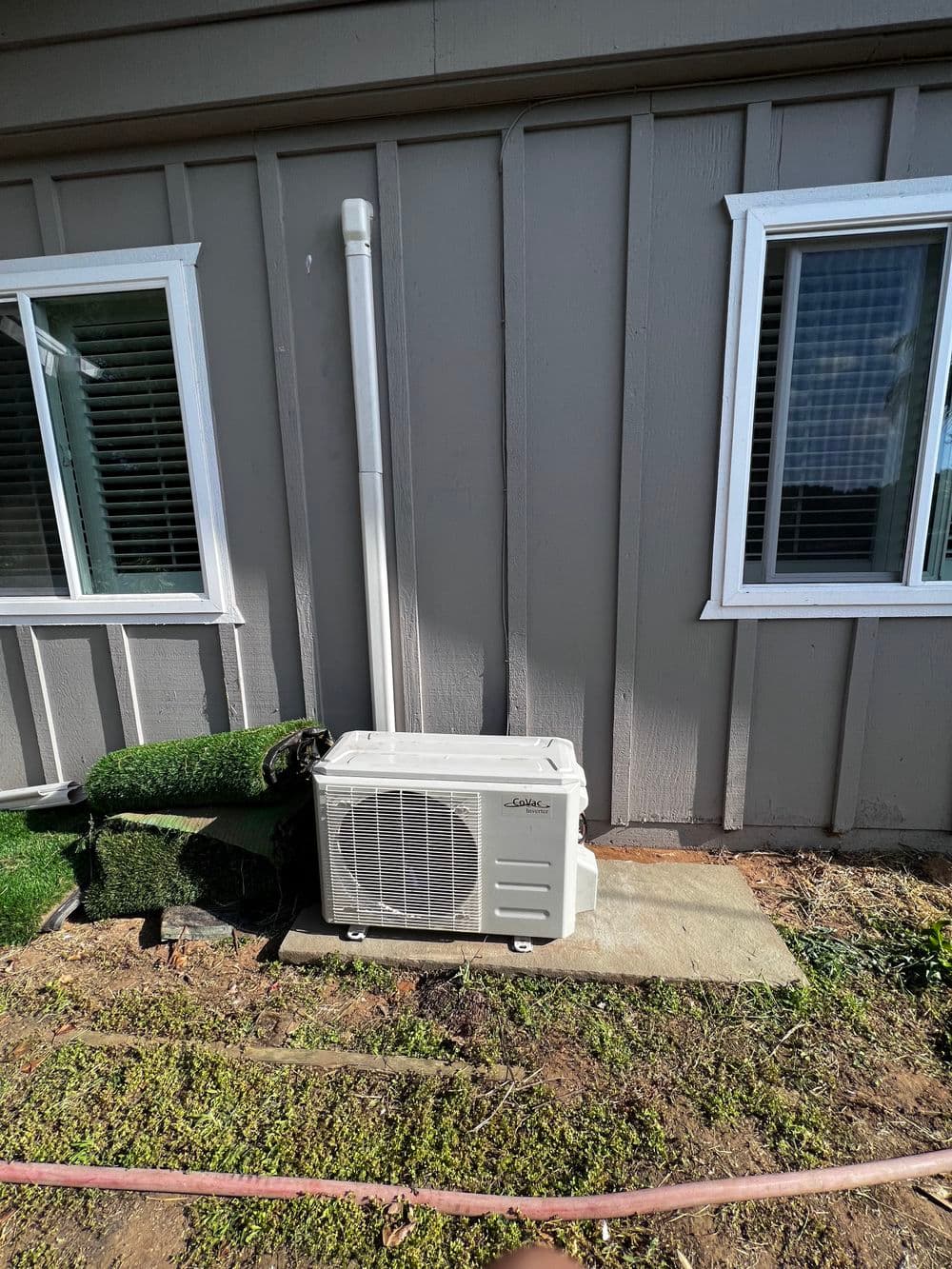 Outdoor air conditioning unit installed beside a textured wall with windows.