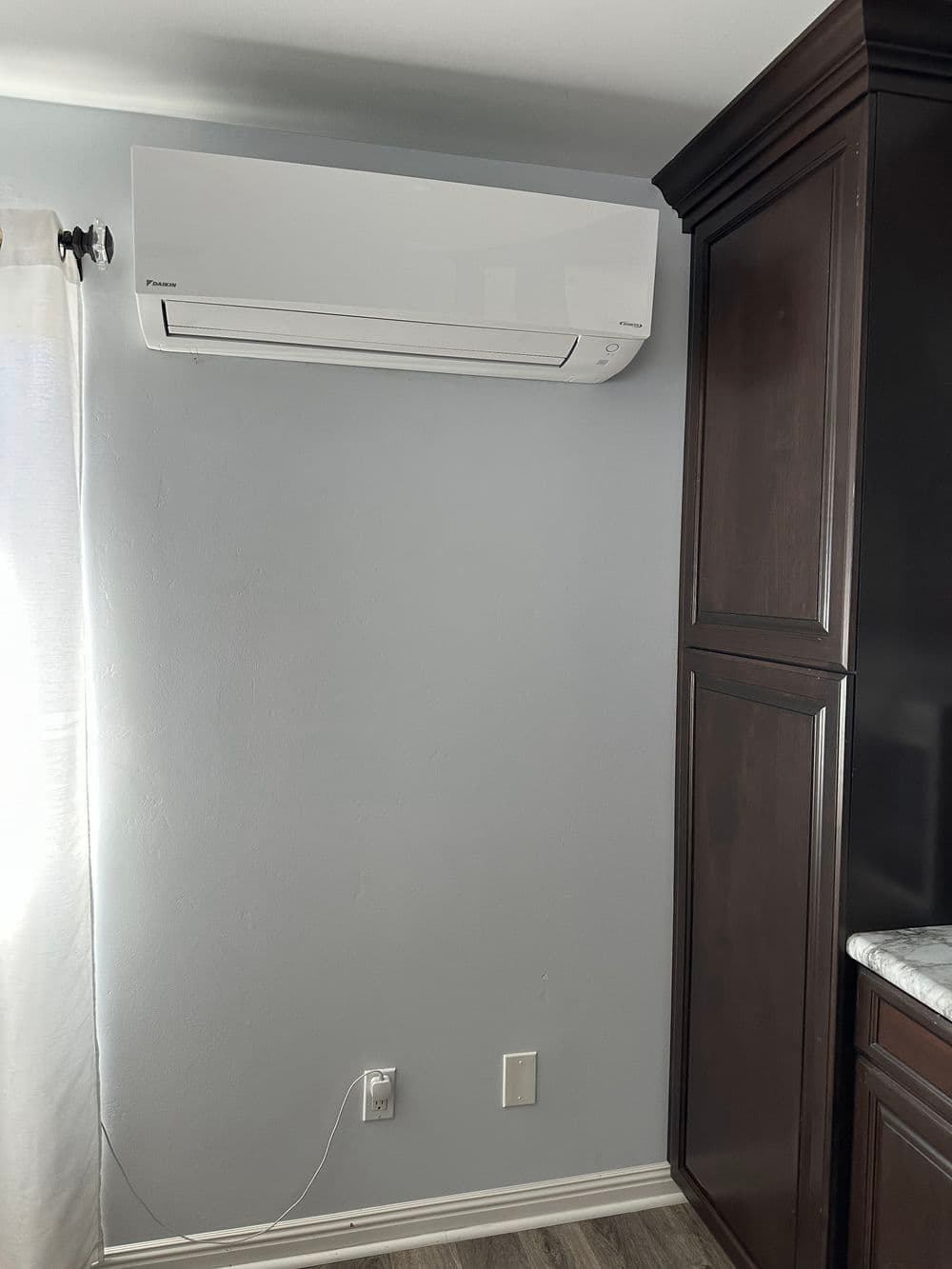 Wall-mounted air conditioner unit in modern kitchen with gray walls and dark wood cabinetry.