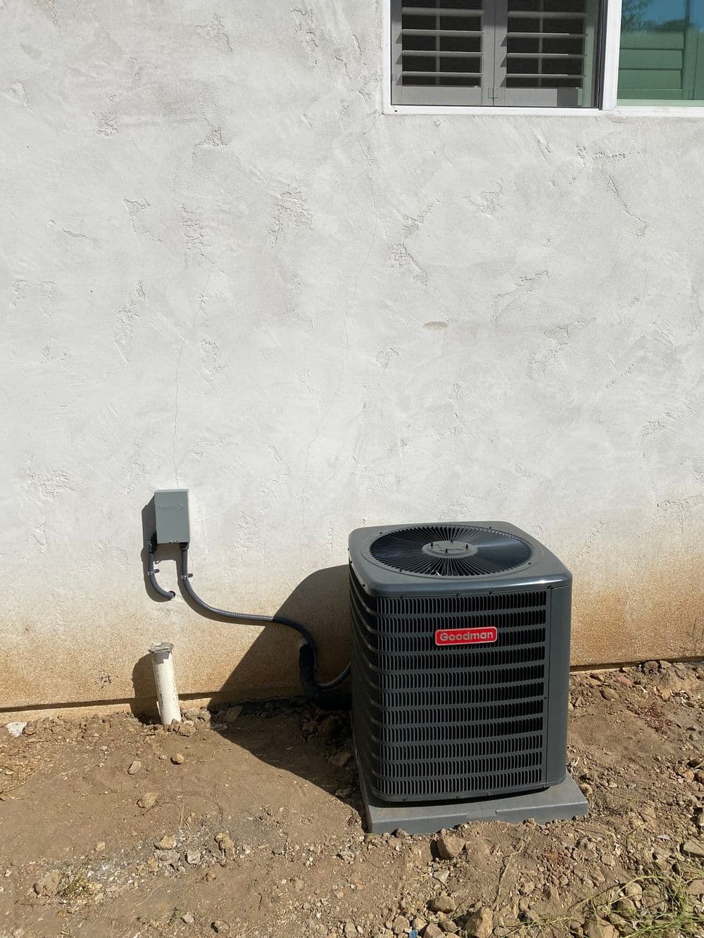 Air conditioning unit installed on exterior wall with electrical connection.