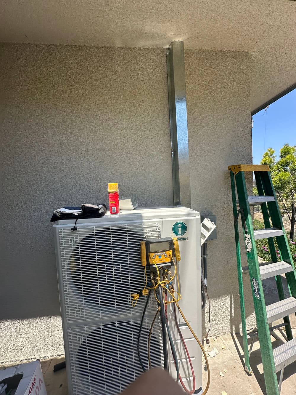 Air conditioning unit with tools and ladder, installed against a textured wall.