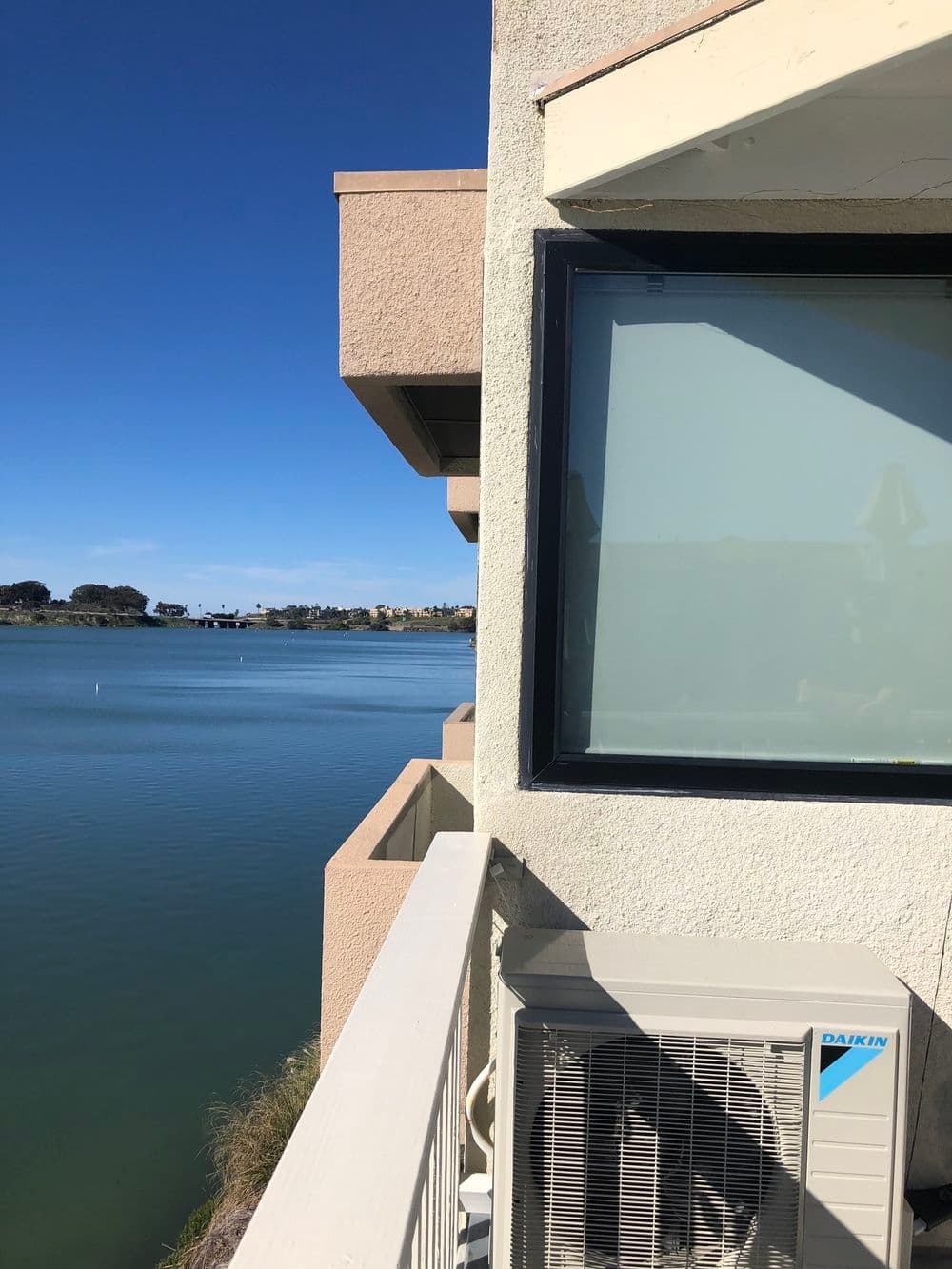 Lakefront view from a building balcony with a visible air conditioning unit.